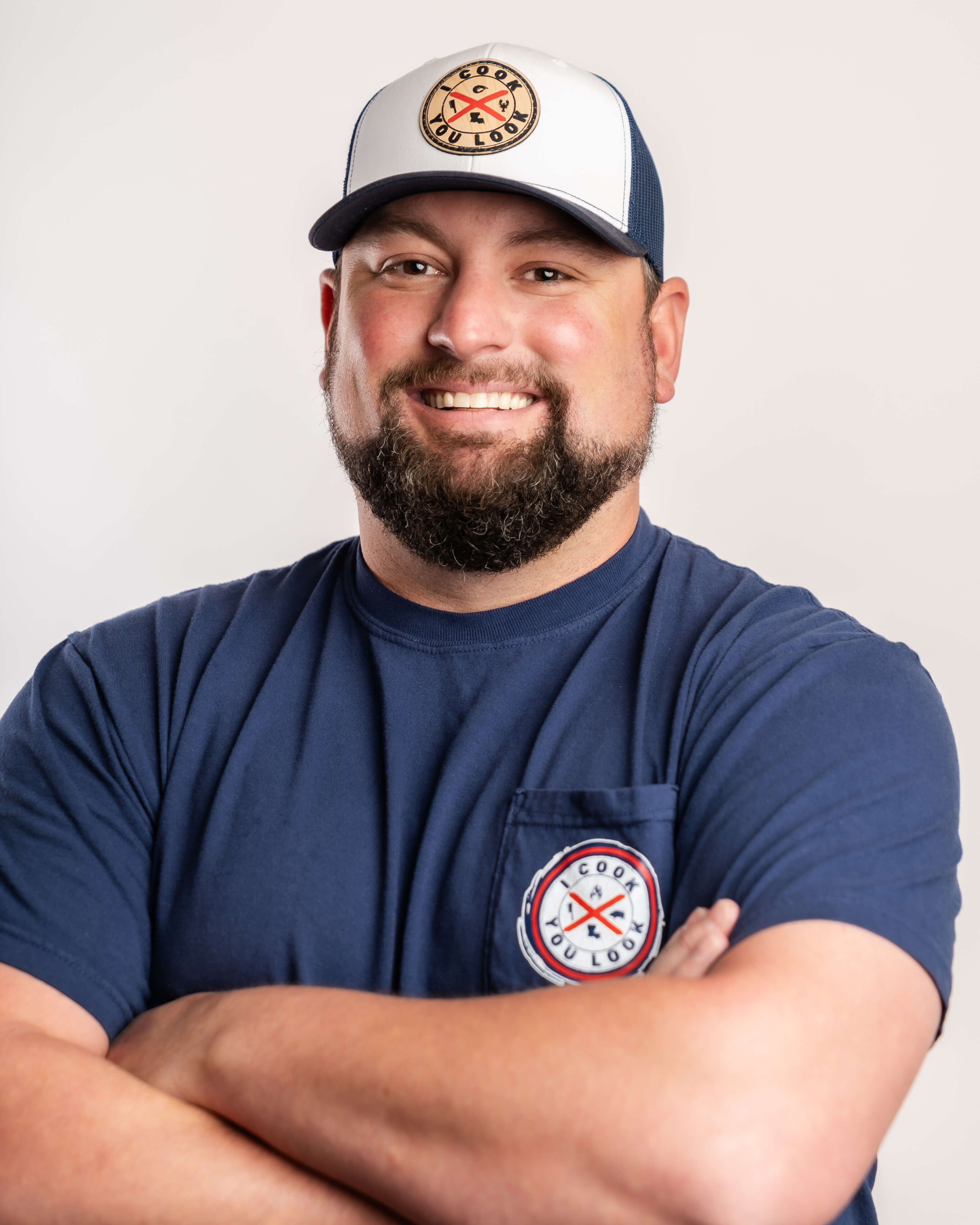 Square format portrait of Austin Dennis, I Cook You Look owner, modeling branded trucker hat and pocket tee.